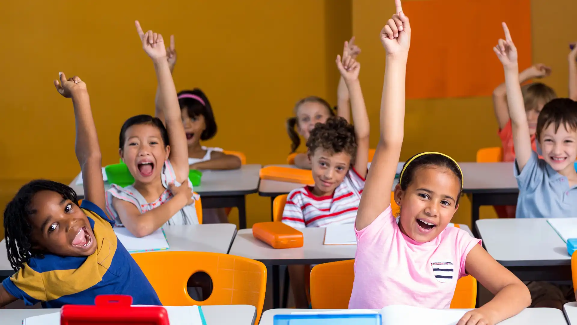Happy children raising their hands in classroom using durable education furniture